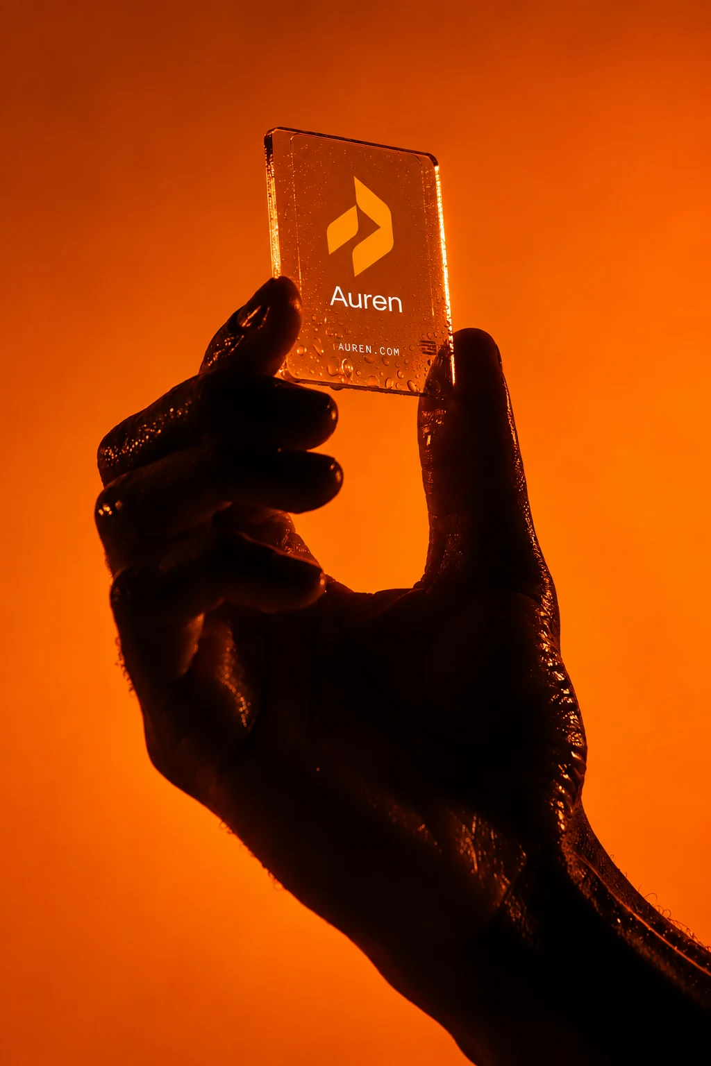 A hand holding a translucent orange Auren card with the symbol and wordmark in warm orange light.