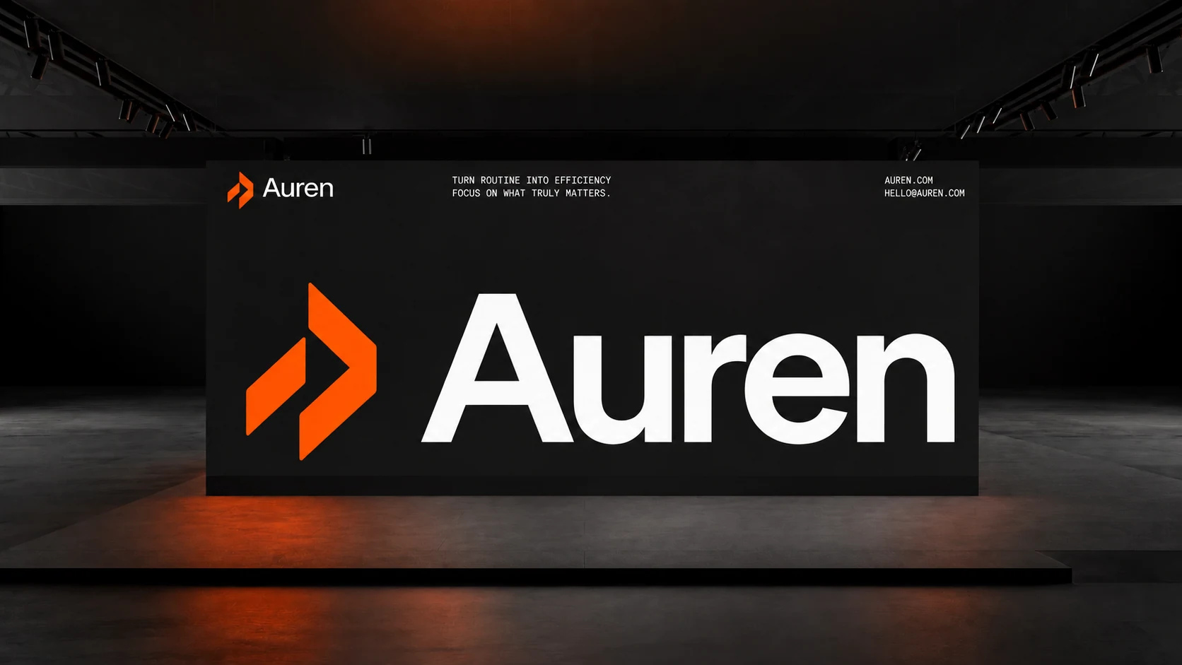 A large orange Auren symbol beside the white wordmark on a black wall in a dark exhibition space.